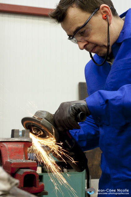 ouvrier homme réalisant un usinage de précision sur une pièce métallique avec une meuleuse et un étau dans l'atelier de mécanique générale admg51