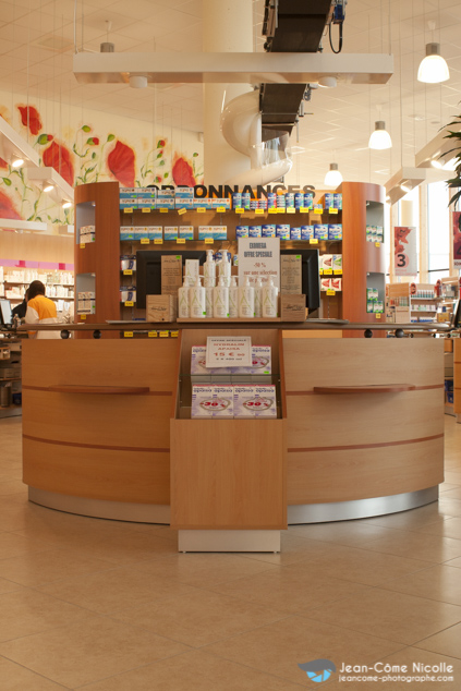 Dans une pharmacie, un comptoir en demi-cercle. une tête de gondole permet de proposer des offres spéciales sur des produits à fort potentiel