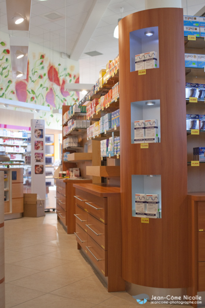 Dans une pharmacie, derrière un comptoir, une étagère chargée de médicaments avec un corner mettant en valeur des produits en promotion